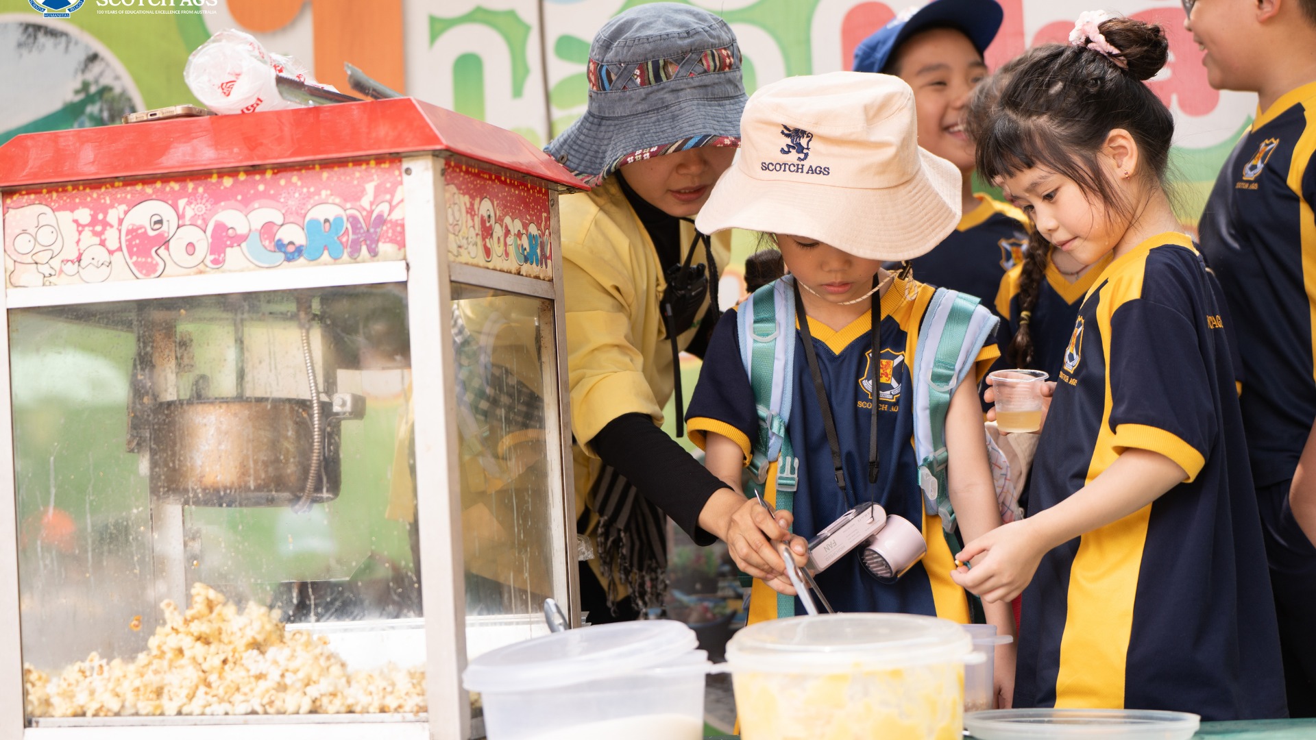 Học sinh Tiểu Học trường Nam Úc Scotch AGS đang tham gia hoạt động bán bắp rang bơ với người bán hàng trong chuyến đi thực tế (field trip)