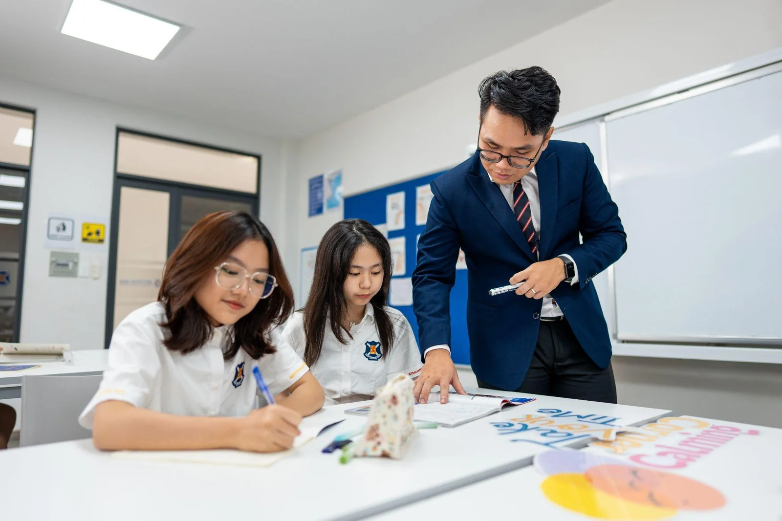 Giáo viên hướng dẫn hai học sinh làm bài trong lớp, minh họa đánh giá xuyên suốt học kỳ
