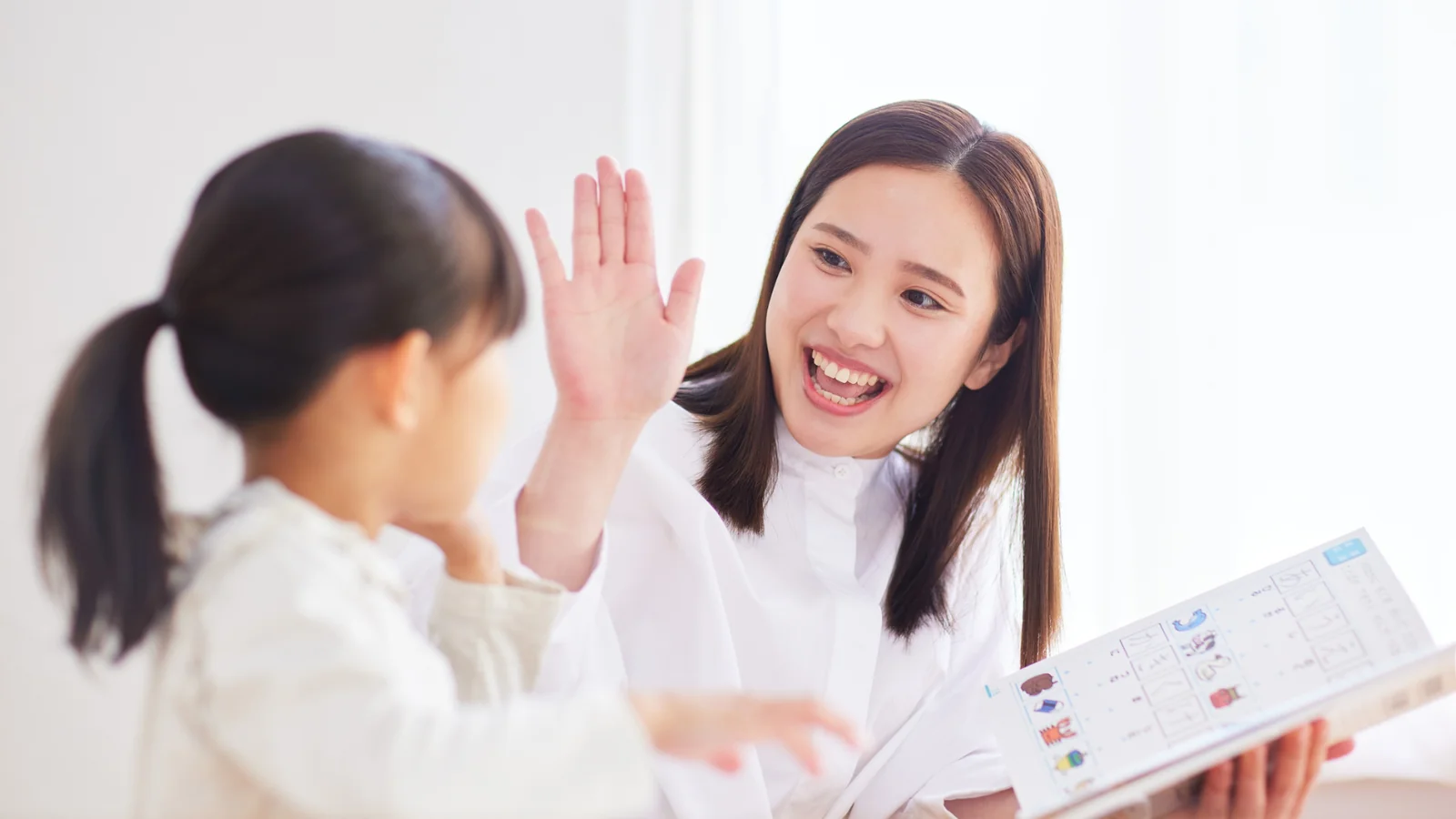 Người lớn đập tay khích lệ bé gái trong lúc cùng xem một cuốn sách, minh họa cách ba mẹ đồng hành cùng con